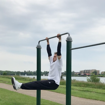 Guy Performing L-sit on Pull Up Bar Flips Weight Plate With Legs